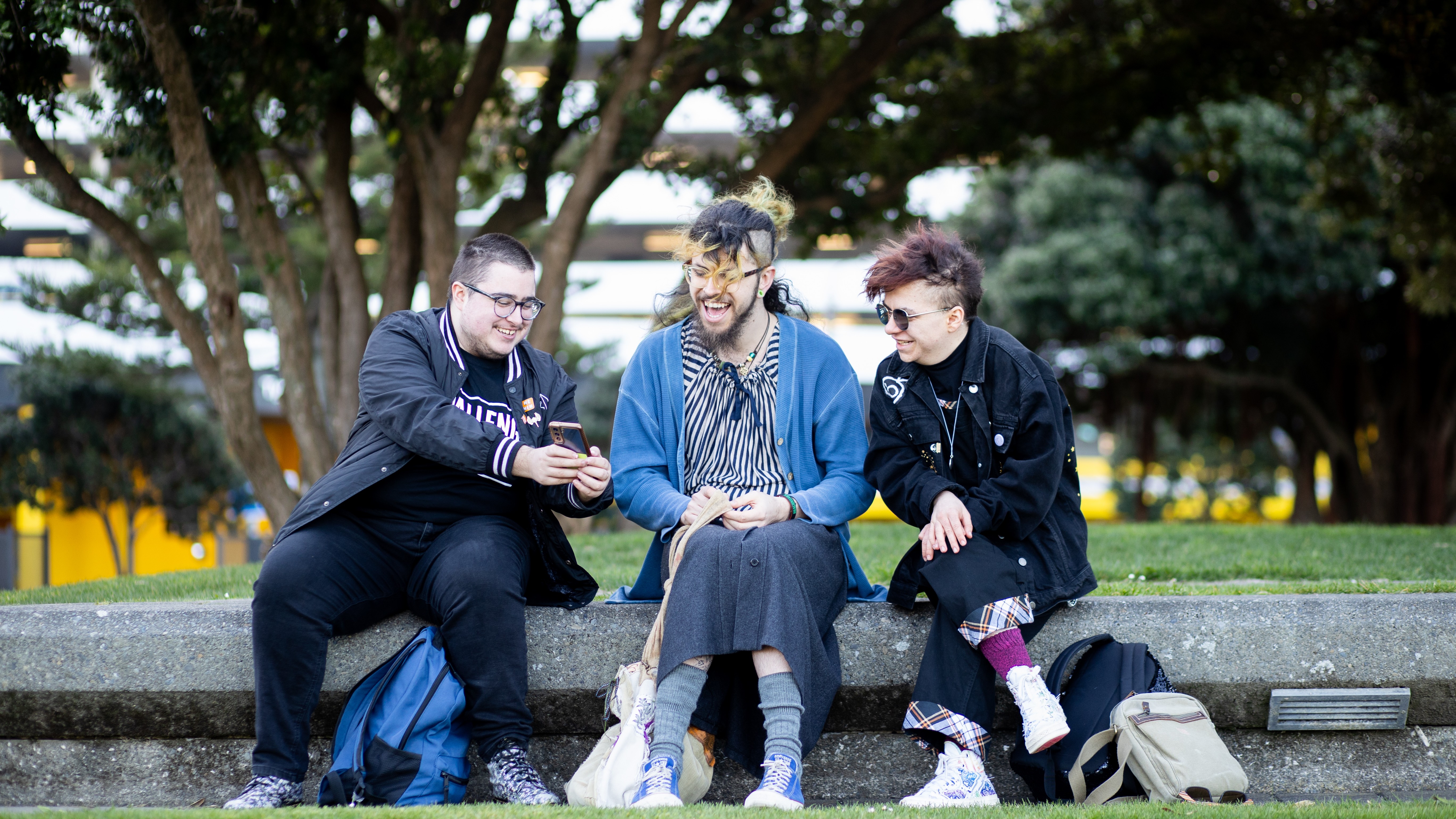 3 young people sitting and laughing together in a park