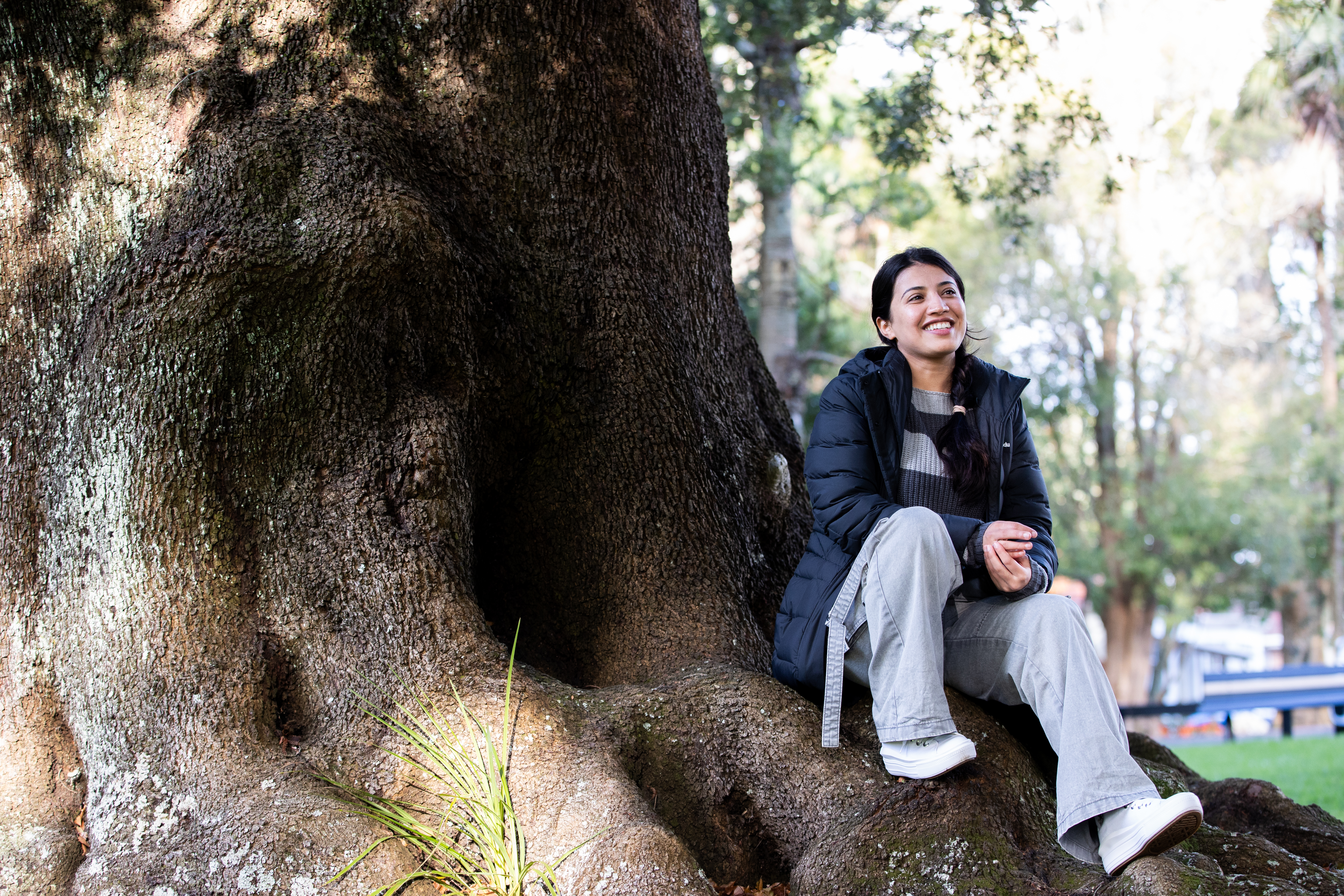 Ethnic female sitting at the base of a tree in a park park at a football game
