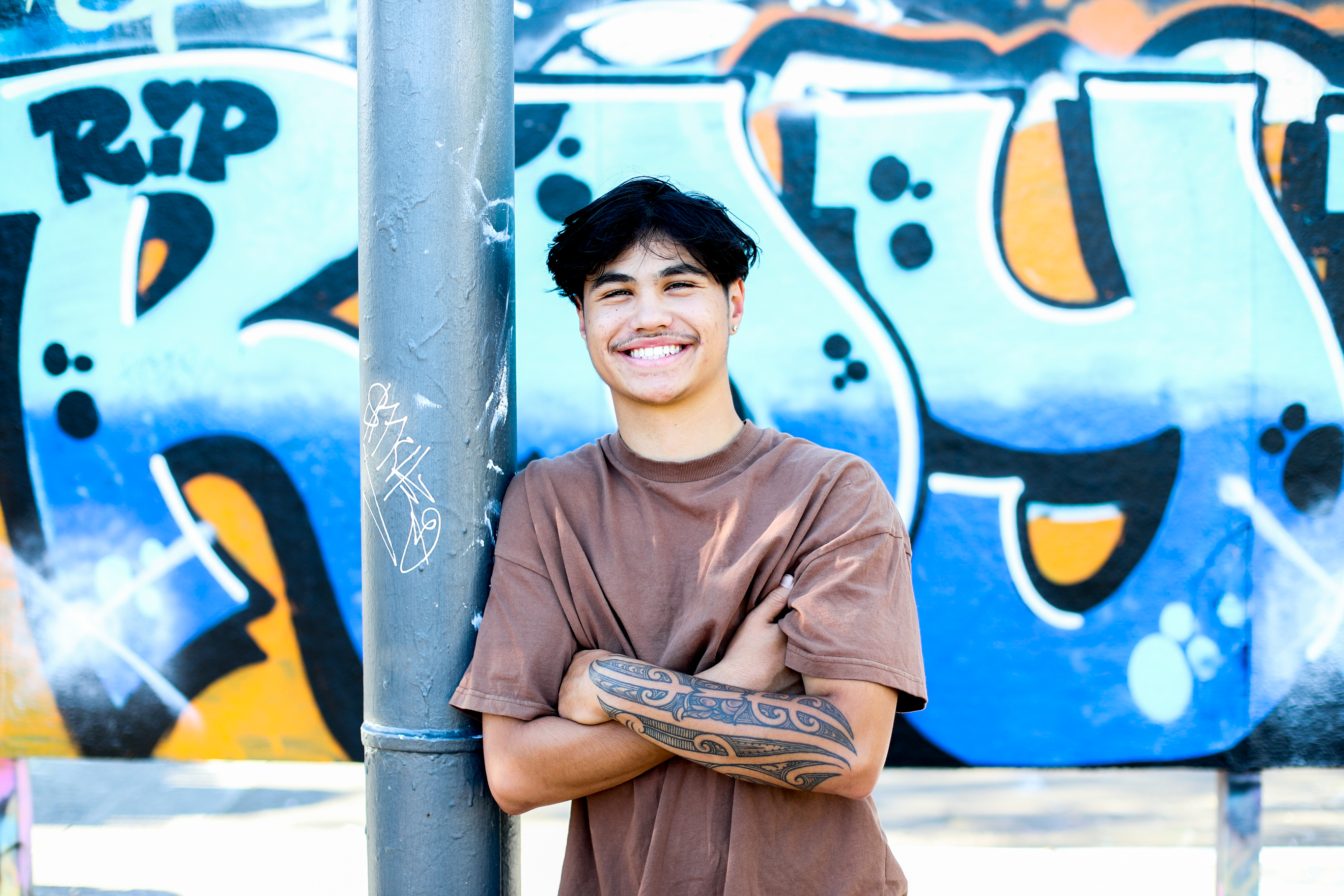 Young person smiles leaning against a pole 