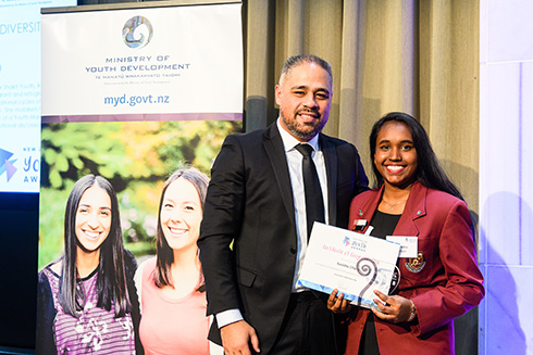 Peeni Henare and Ranisha Chang, holding a certificate, stand to the side of a Ministry of Youth Development banner.