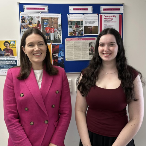 Mikaela Renner, smiling, stands with Hon Brooke van Velden in front of a community notice boad