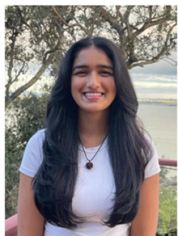 Aanya Shukla smiles at the camera, standing on a balcony looking out to the sea