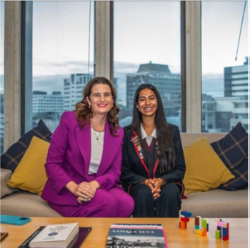 Youth MP Aarthi Candadai and Hon Nicola Willis sit on a couch smiling, the city of Wellington can be seen through the window behind them
