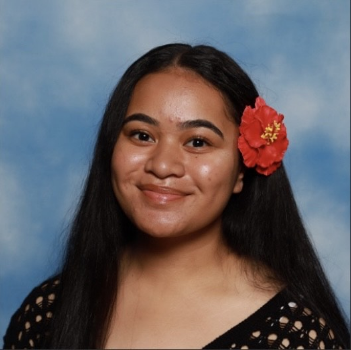 Arunita Vaotuua smiles in front of a plain blue background, a red flower in her hair
