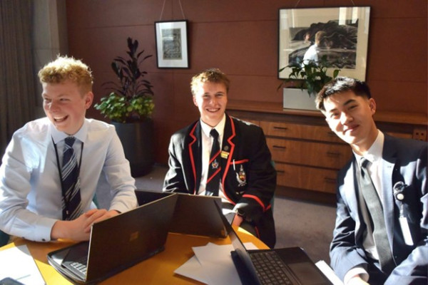 Ben Coull, Hunter Heath, and Daniel Zhao sit smiling around a table