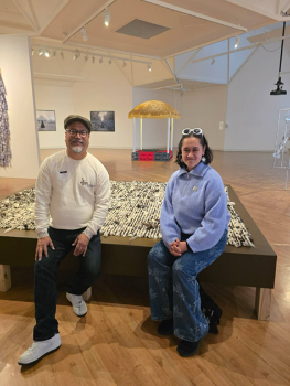 Kaiata Kaitao and Teanau Tuiono sit smiling on a bench inside an art gallery