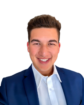 Nikau Adams smiles in front of a plain white background. He is wearing a navy blue blazer with a white undershirt.