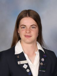 Youth MP Olivia Kelly smiling in her school uniform against a blue backdrop