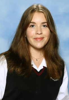 Sophia Blacklock wears her school uniform and smiles in front of a plain blue background